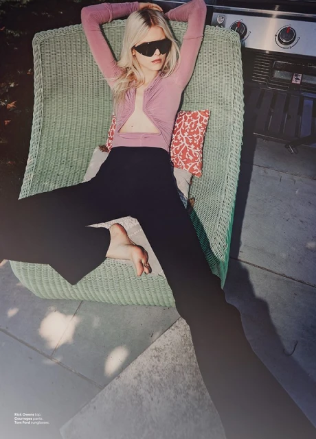 Woman in sunglasses reclines in a wicker chair on a patio, wearing a pink top and dark pants, with a grill visible in the background.