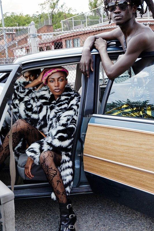 Two fashion models in a car. One is in a zebra print coat and black tights. The other leans in the door in sunglasses.