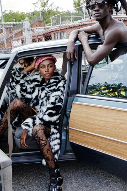 Two fashion models in a car. One is in a zebra print coat and black tights. The other leans in the door in sunglasses.