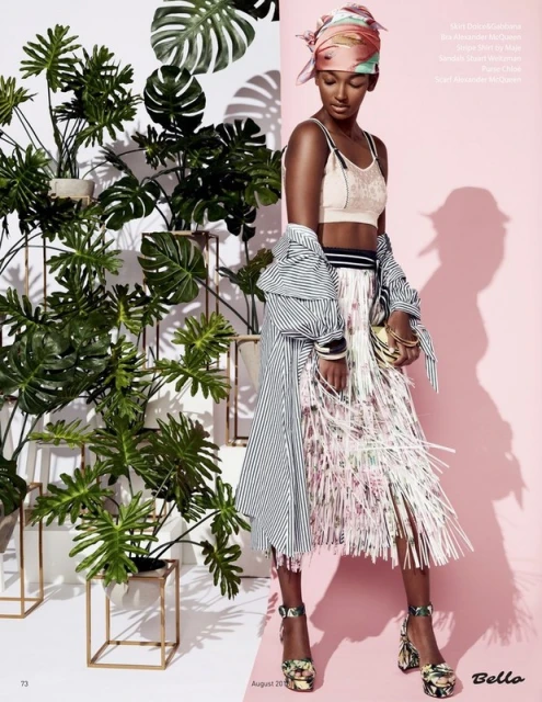 Fashion editorial featuring a young woman in a designer outfit posing against a pink and white wall with tropical plants.