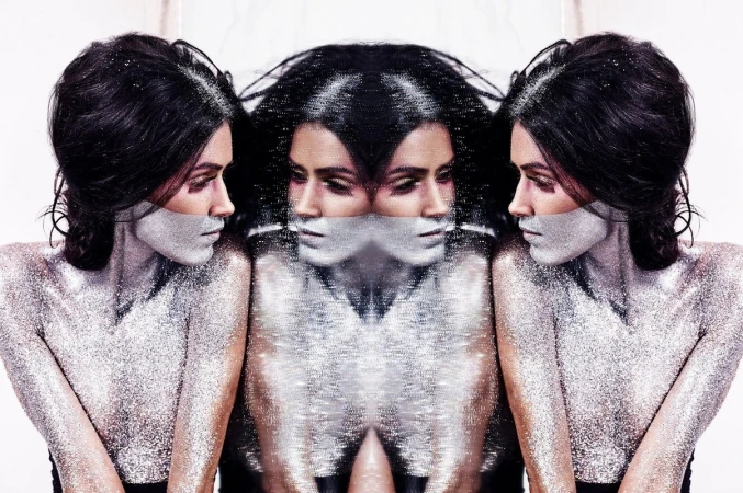 Woman with dramatic silver glitter makeup in a studio photo, mirrored reflections on either side, creating a surreal, beauty-focused aesthetic.