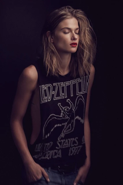 Young woman with closed eyes wearing a Led Zeppelin tank top poses indoors with dark background and moody lighting. Red lipstick.