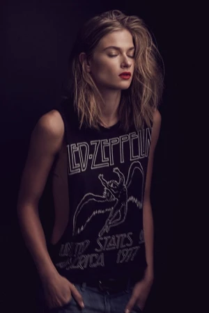 Young woman with closed eyes wearing a Led Zeppelin tank top poses indoors with dark background and moody lighting. Red lipstick.