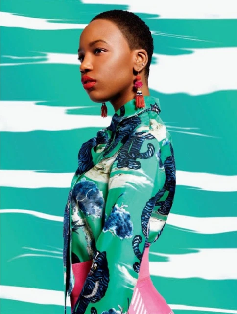 Side view of an adult female model with short hair wearing a patterned button-down shirt against an abstract turquoise and white background.