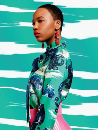 Side view of an adult female model with short hair wearing a patterned button-down shirt against an abstract turquoise and white background.