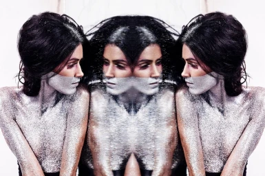 Symmetrical mirrored portrait of a woman with dark hair and silver glitter makeup on her face and shoulders