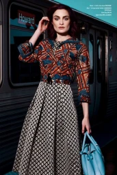 Woman in patterned top and printed skirt holding a blue handbag in front of a subway train in Los Angeles