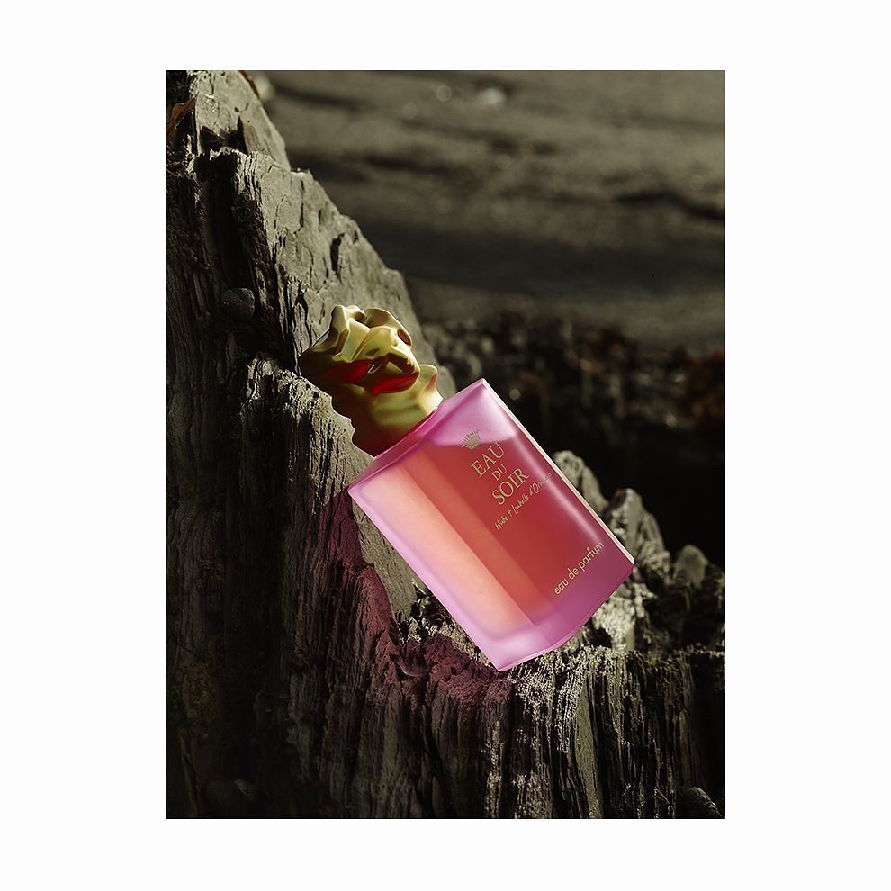 Sisley Eau du Soir perfume bottle on a rough rock surface, studio lighting, product shot, luxury fragrance, textured background, golden lid.