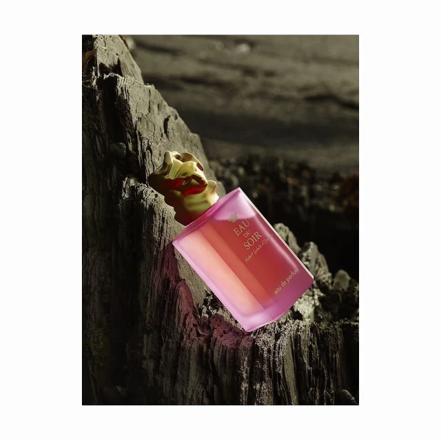 Sisley Eau du Soir perfume bottle on a rough rock surface, studio lighting, product shot, luxury fragrance, textured background, golden lid.