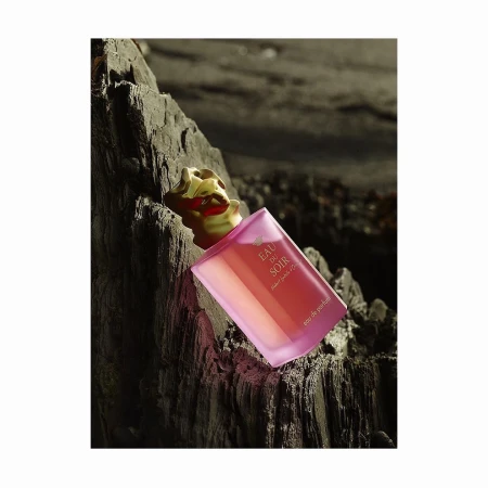 Sisley Eau du Soir perfume bottle on a rough rock surface, studio lighting, product shot, luxury fragrance, textured background, golden lid.