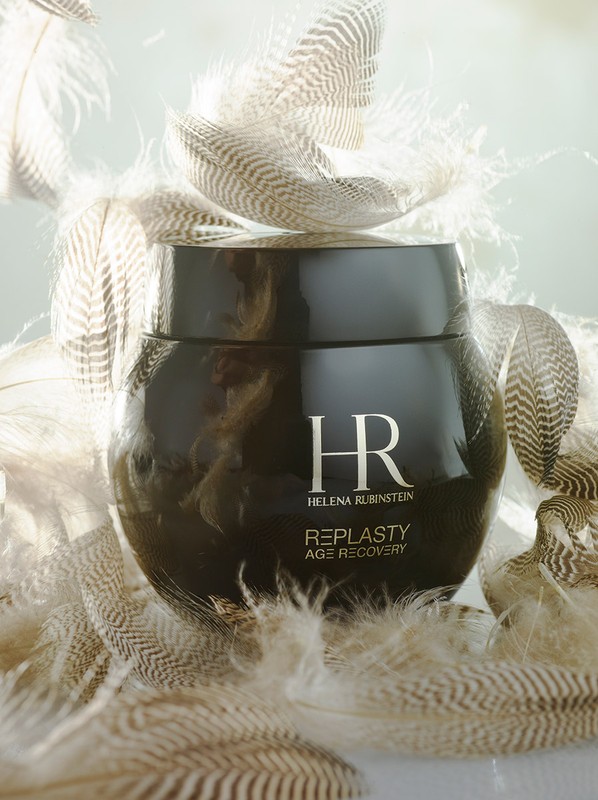 Studio shot of a dark brown jar of Helena Rubinstein Re-Plasty Age Recovery cream surrounded by light brown and white feathers.