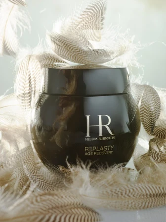 Studio shot of a dark brown jar of Helena Rubinstein Re-Plasty Age Recovery cream surrounded by light brown and white feathers.