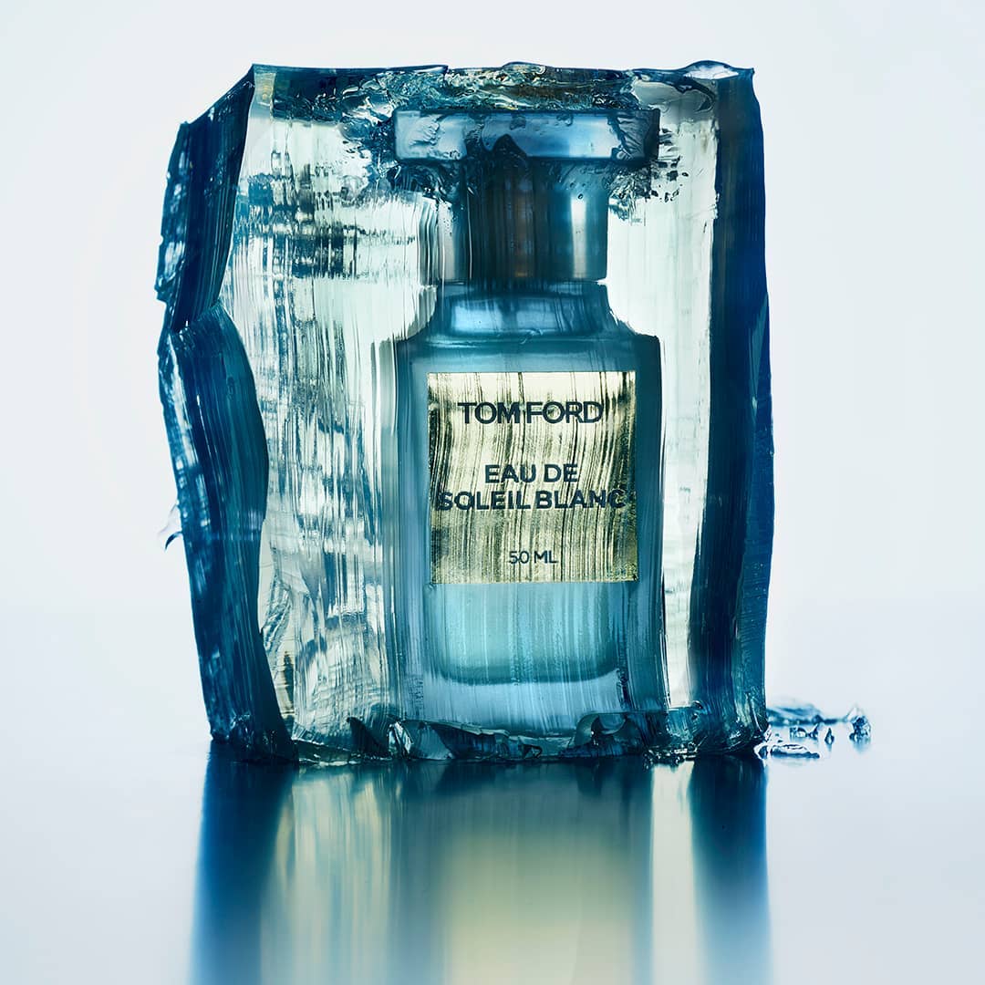 Tom Ford Eau de Soleil Blanc perfume bottle encased in ice, presented against a soft white background with reflective surface.