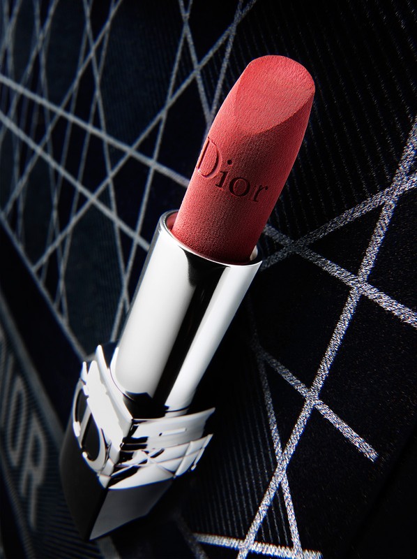Close-up of a red Dior lipstick in a silver and black tube against a dark patterned background shot by Graeme Montgomery.