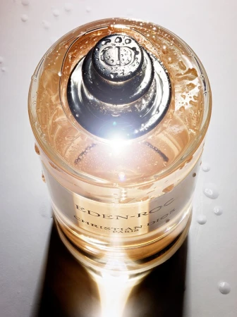 Close-up studio shot of a clear, glass Christian Dior Eden-Roc perfume bottle with a silver applicator, highlighted by bright lighting.