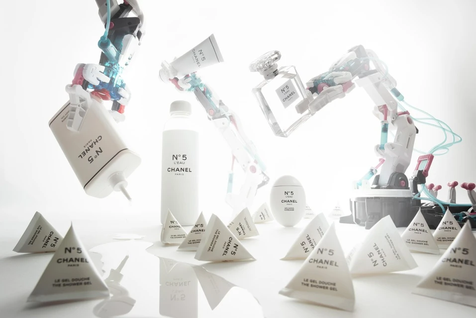 Shot of Chanel N°5 product collection with robot arms on white backdrop. Cosmetics include perfume, shower gel, lotion, body cream, and robot arms.