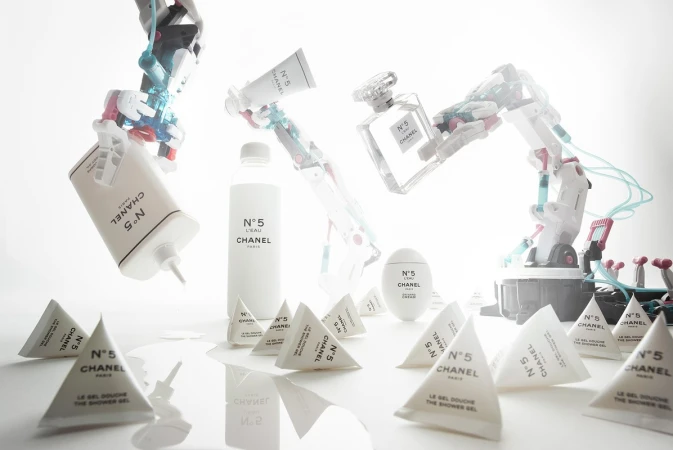 Shot of Chanel N°5 product collection with robot arms on white backdrop. Cosmetics include perfume, shower gel, lotion, body cream, and robot arms.