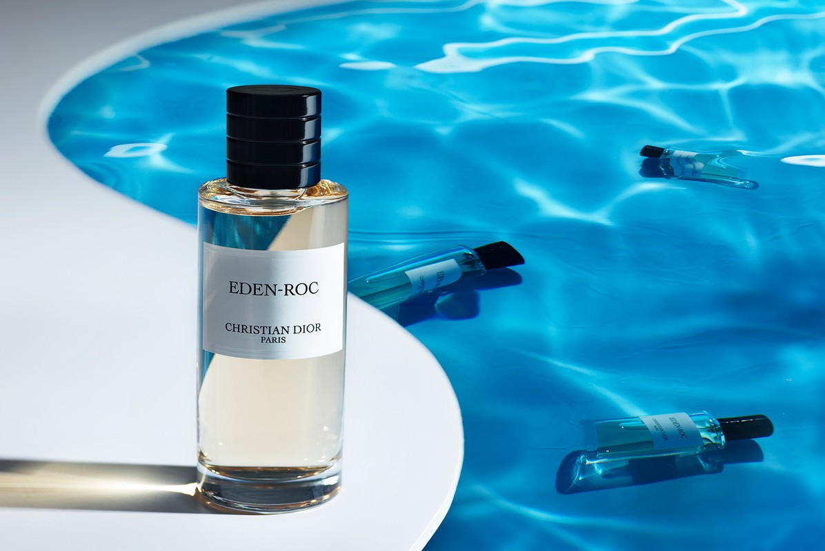 Christian Dior Eden-Roc perfume bottle centered on a white surface, surrounded by several floating sample vials in blue water.