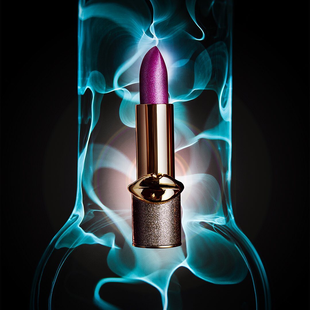 Close-up shot of a purple lipstick tube in front of blurred blue and white background, product shot for beauty or cosmetic.