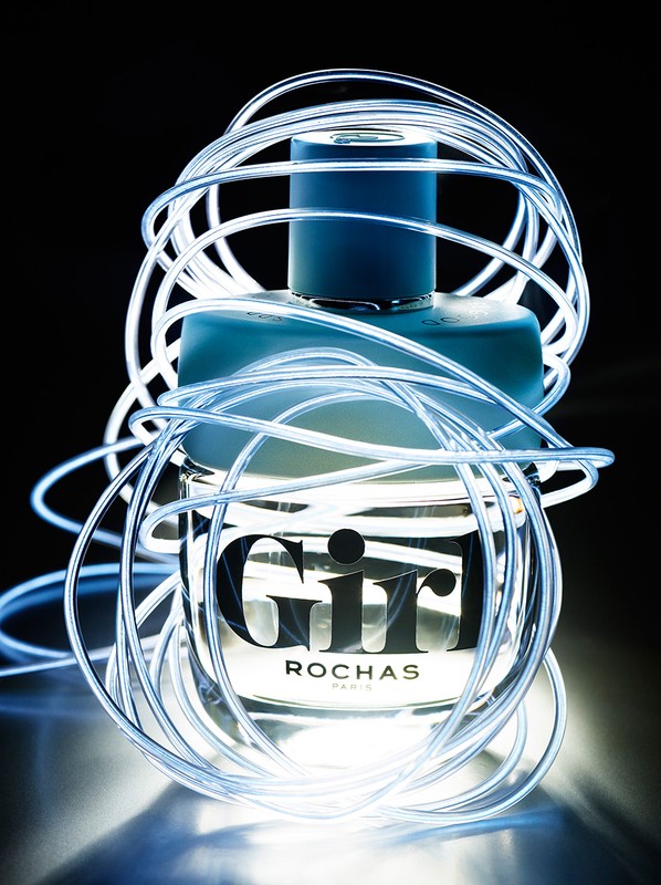 Rochas 'Girl' perfume bottle captured in a studio shot, encircled by glowing, flexible LED light tubes, set against a dark backdrop.