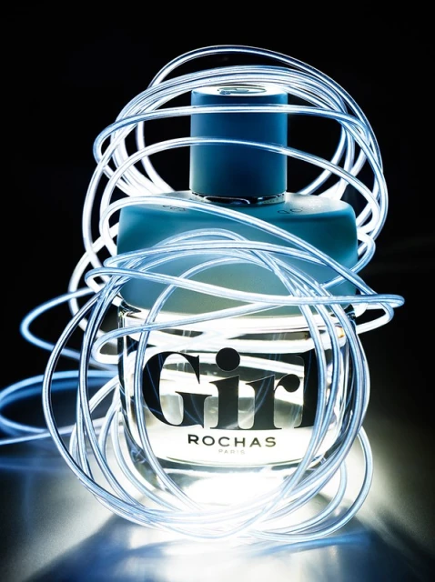 Rochas 'Girl' perfume bottle captured in a studio shot, encircled by glowing, flexible LED light tubes, set against a dark backdrop.