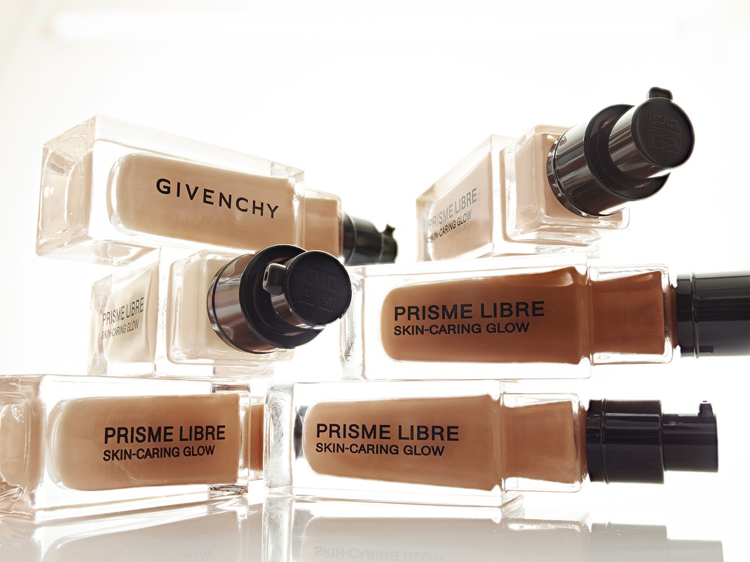 Stack of Givenchy Prisme Libre skin-caring glow foundations in clear glass bottles with black pumps against a white background.
