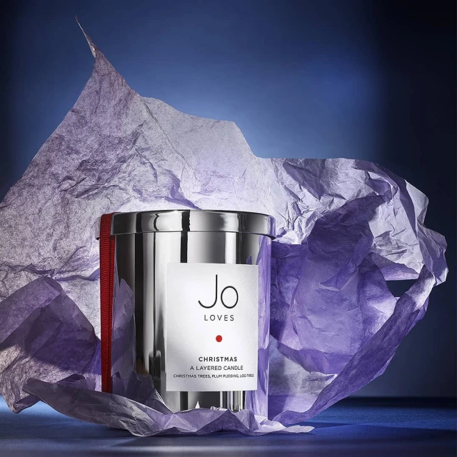 Jo Loves Christmas layered candle in a silver metal container wrapped in red ribbon, with crumpled light purple tissue paper.