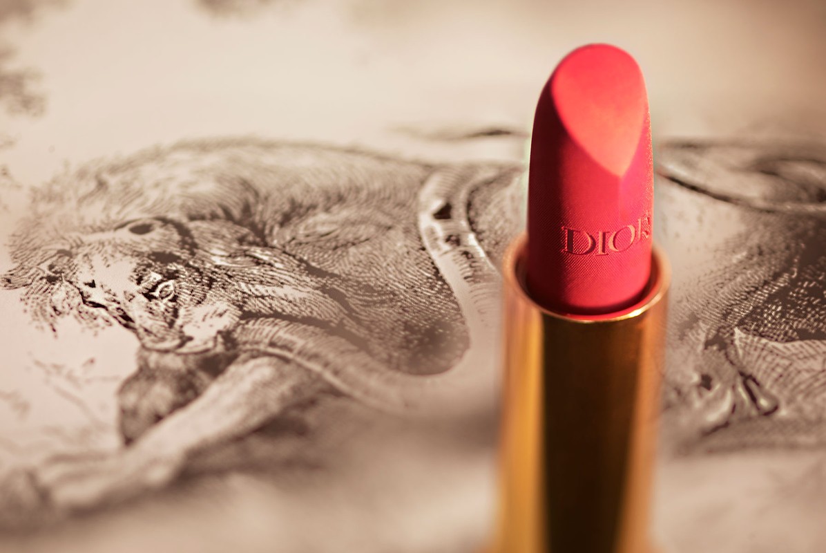 Close-up of red lipstick with gold tube, featuring the Dior logo, against a backdrop with a vintage lion sketch illustration.