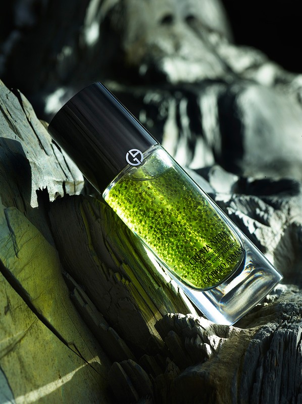 Cylindrical glass skincare bottle containing green liquid resting vertically against weathered dark wood texture