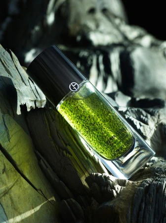 Cylindrical glass skincare bottle containing green liquid resting vertically against weathered dark wood texture
