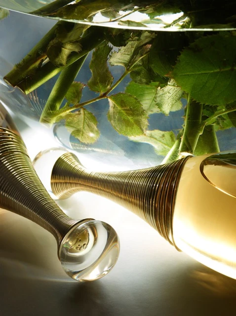 Luxury perfume bottles arranged elegantly next to rose stems in glass. Warm light creates a sophisticated, inviting ambiance.