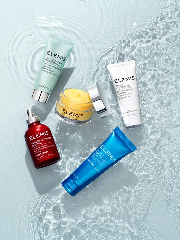 Cosmetic products from ELEMIS are arranged on a bright blue surface with water ripple effects, showcasing skincare and body care.