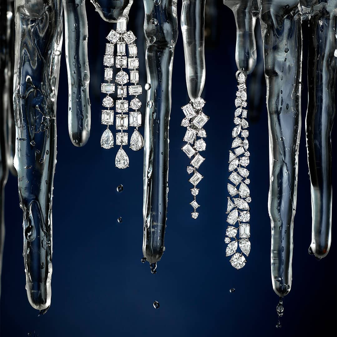 Elegant diamond earrings hanging from icicles against a dark blue background. Jewelry concept with a cold, luxurious aesthetic.