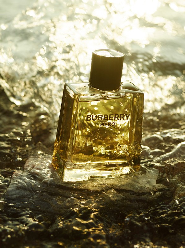 Burberry Hero fragrance bottle on a wet rock surface with golden water reflections. Product photography showcasing luxury perfume.