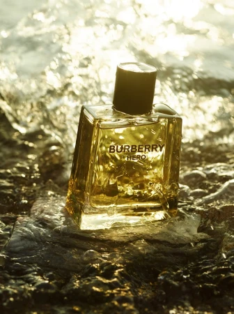 Burberry Hero fragrance bottle on a wet rock surface with golden water reflections. Product photography showcasing luxury perfume.