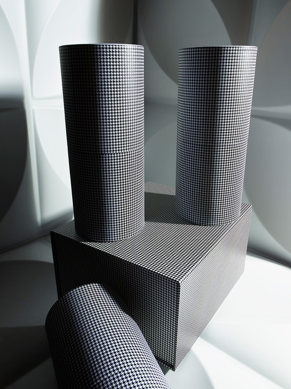 Geometric product shot featuring three cylinders and a rectangle covered in houndstooth pattern set against a white patterned background.