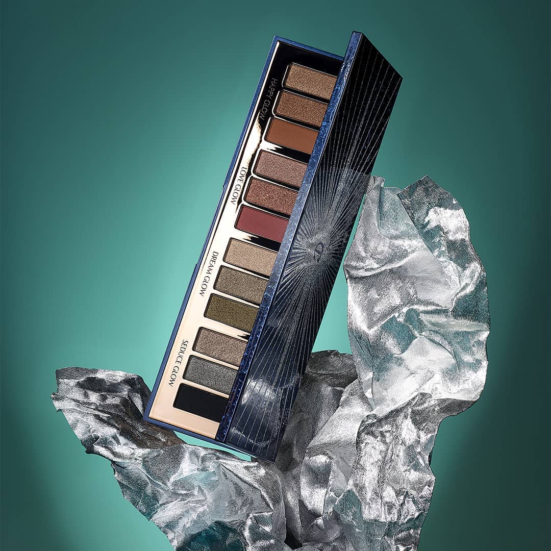 Eye shadow palette by Charlotte Tilbury on silver crinkled material against a teal background in a beauty product shot.