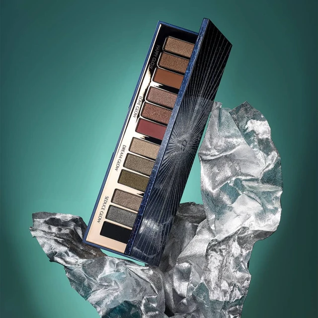 Eye shadow palette by Charlotte Tilbury on silver crinkled material against a teal background in a beauty product shot.