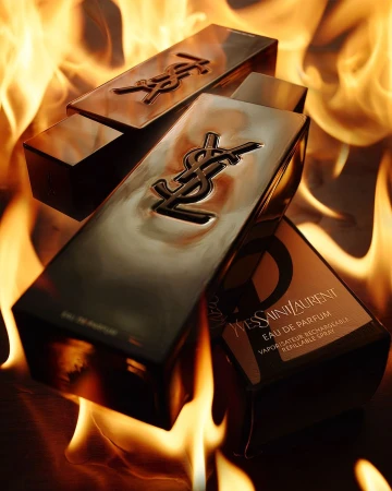 Still life shot of Yves Saint Laurent perfume bottles with the brand logo visible, set against a background of vibrant, blurred flames.