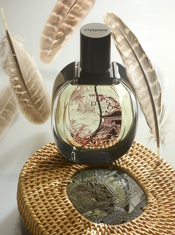 Perfume bottle on a woven coaster with feathers in the background. Neutral tones create a sophisticated and minimalist beauty product still life.