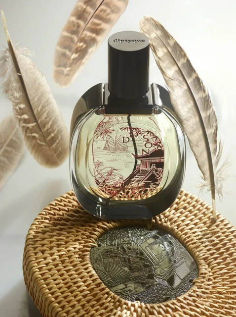 Perfume bottle on a woven coaster with feathers in the background. Neutral tones create a sophisticated and minimalist beauty product still life.