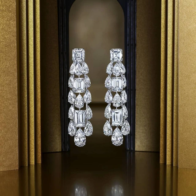 Elegant dangle earrings featuring diamond accents in a detailed, tiered design, showcased against a gold-toned backdrop with soft lighting.