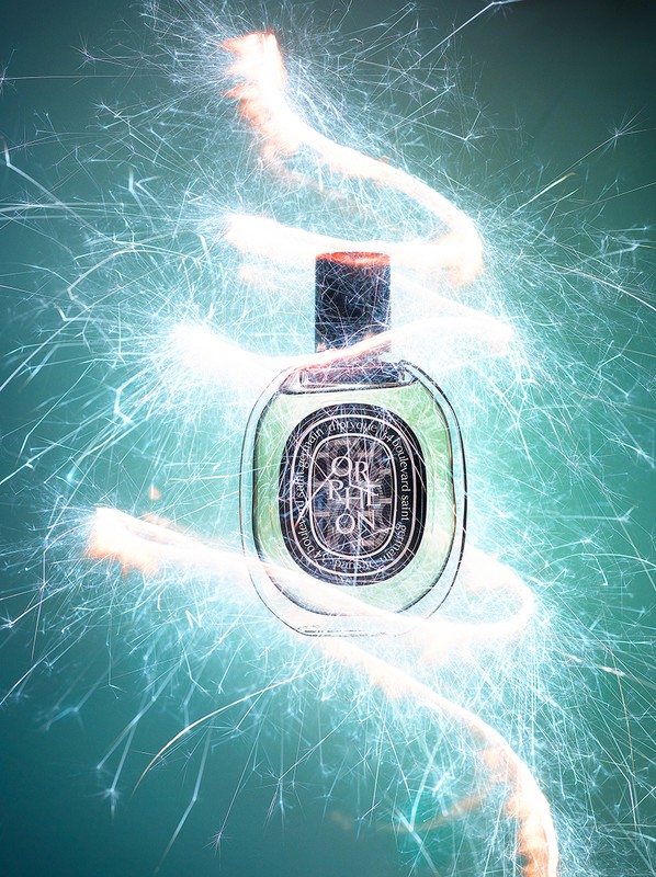 Perfume bottle presentation with light painting effect on teal backdrop. Luxury fragrance spotlight with creative light trails.