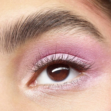 Close-up of a woman's eye with pink eyeshadow and dark brown eyebrow, eyelashes, and eye color against fair skin.