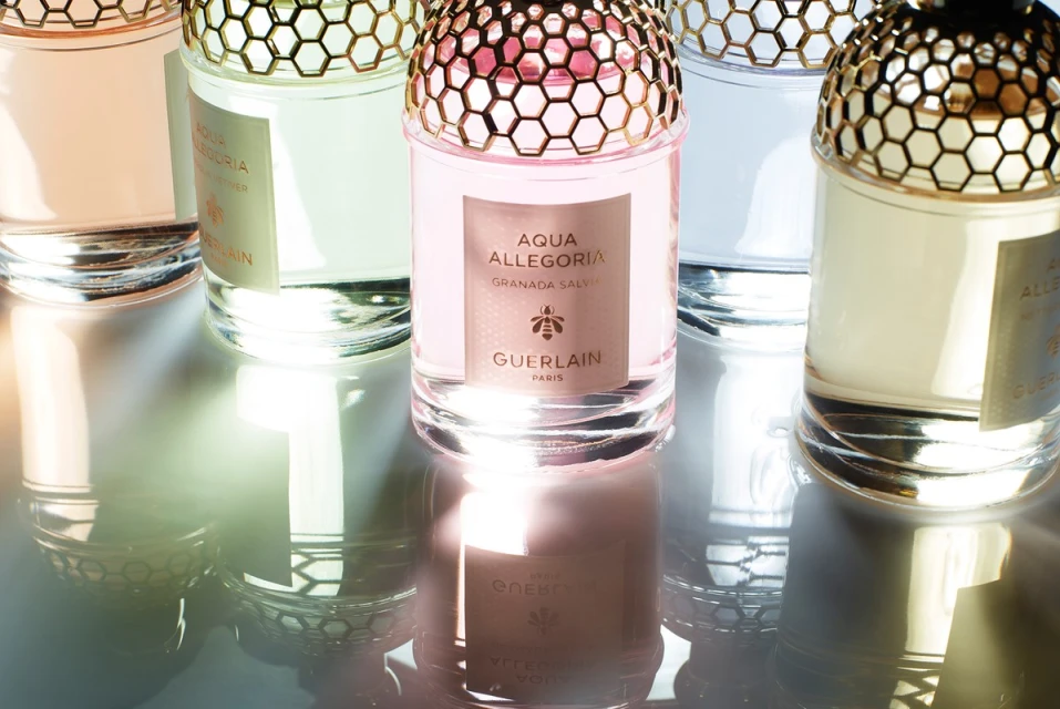 Close-up of various pastel-colored Guerlain Aqua Allegoria perfume bottles with gold honeycomb caps, reflecting on a shiny surface.
