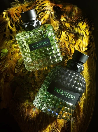 Two faceted Valentino perfume bottles stand on a bed of feathers in a beauty shot with studio lighting.