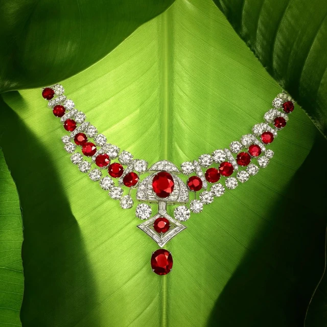 Elegant diamond and ruby necklace displayed on a lush green leaf, showcasing jewelry design and natural beauty in a studio setting.