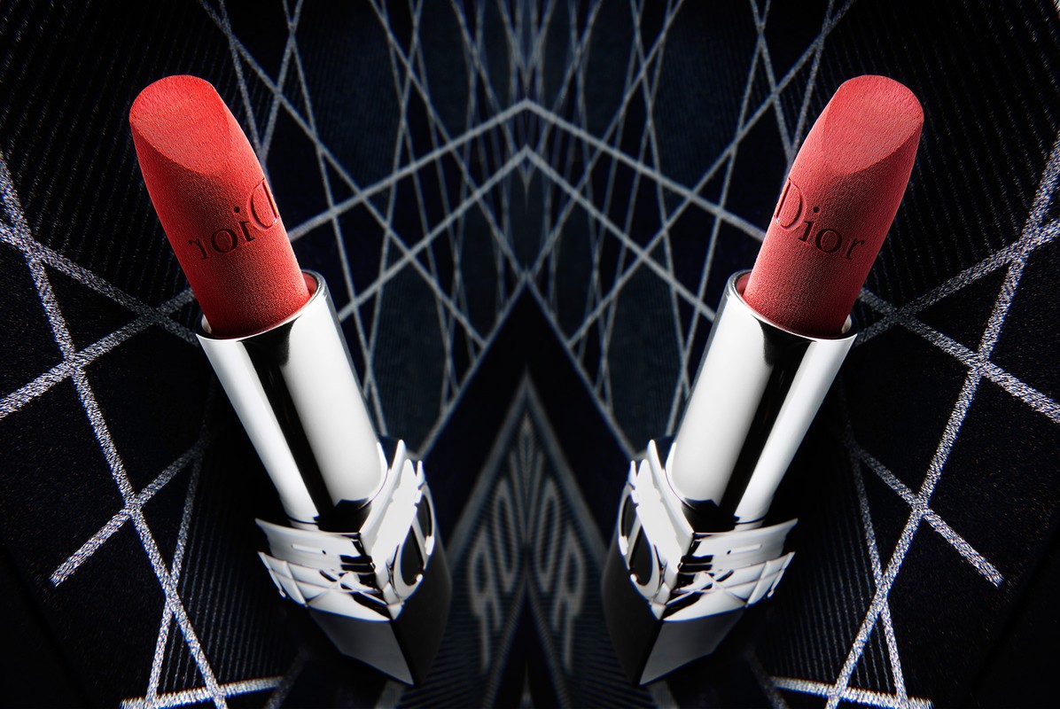 Close-up studio shot of two red Dior lipsticks with silver tubes symmetrically arranged against a dark geometric background.