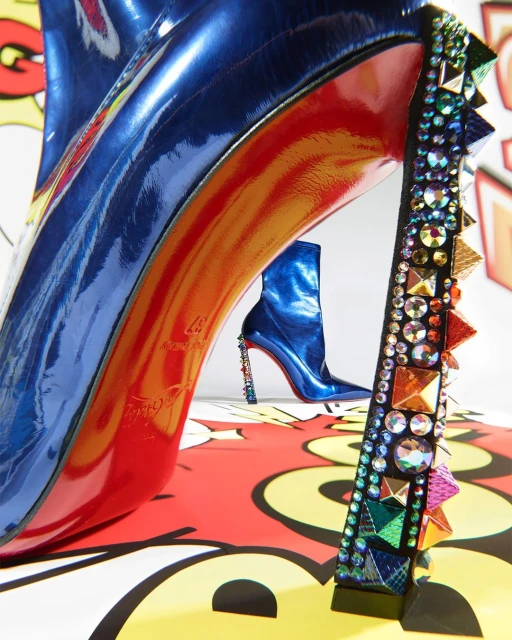 Fashion still life of blue patent leather high heel shoes with jeweled accents and red soles, one a boot and one a pump.