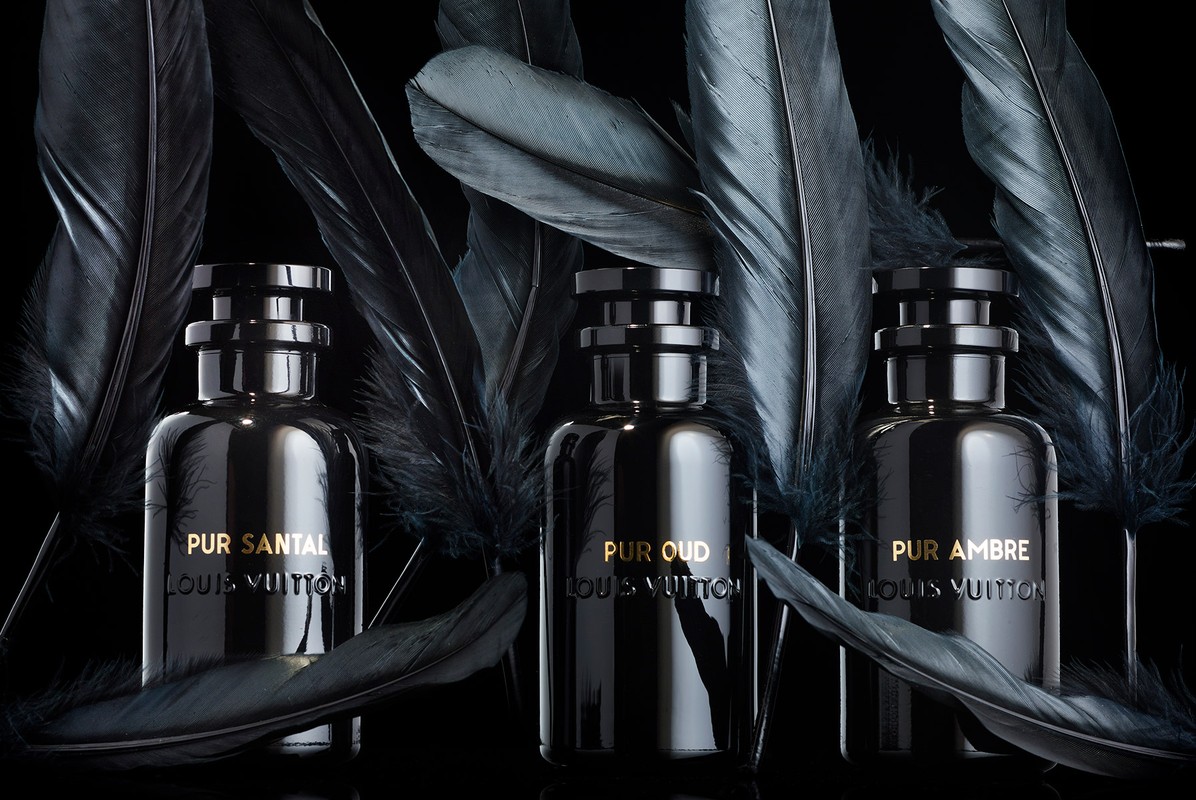 Three dark perfume bottles from Louis Vuitton are displayed with dark feathers against a black background, creating a moody, elegant aesthetic.